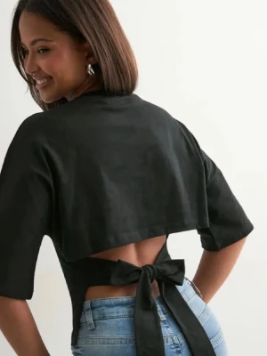 Svart croppad topp med knyt - Trendig svart croppad topp med öppen rygg och breda knytband i midjan. Toppen har korta ärmar och en stilren design som passar perfekt till jeans eller kjol. Snygg detalj med rosett baktill för en extra touch.