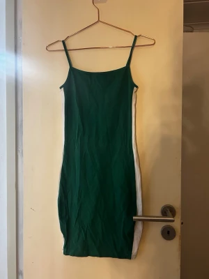 Grön och vit tight klänning - Snygg grön klänning med vita paneler längs sidorna och smala axelband. Tight passform och kort längd, perfekt för en trendig look. Materialet känns mjukt och stretchigt.