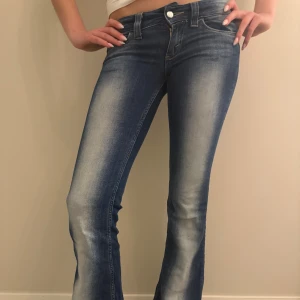 Blå bootcut jeans med slitningar - Säljer ett par blå bootcut jeans med snygga slitningar och ljusa tvättade partier framtill. Jeansen har klassisk femficksdesign, bälteshällor och knappgylf. Materialet är jeans i bomull och passformen är normal med utsvängda ben. Jeansens storlek är 25/32 