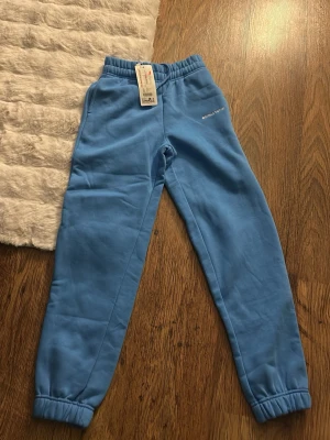 Blå mjukisbyxor från Studio Total - Snygga blå mjukisbyxor från Studio Total med resår i midjan och bensluten. Tillverkade i mjukt bomullsmaterial som känns skönt mot huden. Perfekta för chill eller häng med vänner. Enkel design med liten logga på höften. Stl xxs men passar även S