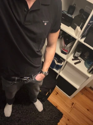 Svart pikétröja från GANT - Klassisk svart pikétröja från GANT med liten logga på bröstet. Tröjan har krage, korta ärmar och knappar vid halsen. Perfekt till jeans eller chinos för en clean och stilren look. Använt 2-3 gånger.