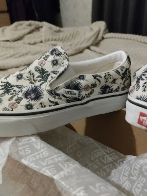 Vans Classic Slip-On Paradise Floral/True White - Säljer ett par vita Vans slip-on sneakers med blommigt mönster i blått, rosa och grönt. Skorna har en klassisk låg profil, elastiska sidor och vit sula med svart rand. Perfekta för dig som vill sticka ut unikt i sommaren. De är använda 2 gånger bara. De säljs inte längre  och är unika limited. 
