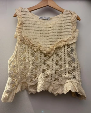 Virkat linne med volang från Zara - Superfint virkat linne i beige från Zara med volangdetaljer och spetskant. Toppen har ett luftigt, mönstrat virkparti och är ärmlös vilket är perfekt till sommaren, då den är luftig och skön! 