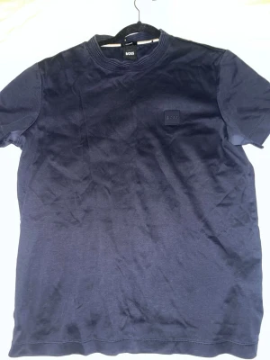 Mörkblå t-shirt från BOSS - Snygg mörkblå t-shirt från BOSS med diskret logga på bröstet. Klassisk rund halsringning och korta ärmar. Tillverkad i mjuk bomull som känns skön mot huden. Perfekt för en clean och stilren look.