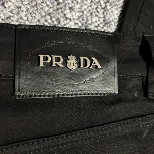Svarta raka jeans från Prada  - Snygga svarta jeans från Prada med klassisk rak passform. Jeansen har diskreta fickor fram och bak samt ett stilrent svart läderpatch med Prada-logga i midjan. Perfekta till alla typer av outfits och tillverkade i ett mjukt bomullsmaterial. Priset kan diskuteras 😊
