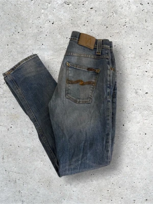 LjusBlå jeans från Nudie Jeans - Säljer ett par klassiska blå jeans från Nudie Jeans i mycket bra skick. Modellen på jeansen är Grim Tim. Jeansen har fem fickor, normal passform och Nudie-loggan broderad på bakfickan. Perfekta till en avslappnad stil och tillverkade i mjuk bomull.