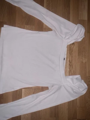 Vit ribbad långärmad topp - Säljer en vit ribbad topp med lång ärm och fyrkantig ringning. Toppen har en slim passform och är tillverkad i ett mjukt, stretchigt material som passar perfekt till jeans eller kjol. Enkel men stilren design som är lätt att matcha.
