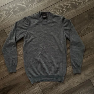 Grå stickad tröja  - Mjuk och stilren grå stickad tröja från Oscar Jacobson i klassisk modell. Tröjan har rund halsringning, långa ärmar och ribbade muddar vid ärmslut och nederkant. Perfekt för lager på lager och enkel att matcha med olika outfits. Fri frakt