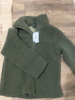 Olivgrön teddyjacka från Gina Tricot - Mysig olivgrön teddyjacka från Gina Tricot med hög krage och dragkedja framtill. Jackan är gjord i fluffigt teddy-material och har en relaxed passform som passar perfekt till kalla dagar. Jackan är helt ny med prislapp kvar! Pris går att diskutera!💕