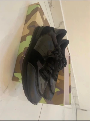 Svarta Valentino Garavani sneakers - Snygga svarta Valentino Garavani sneakers med klassisk siluett. Skorna har en mix av skinn och textil, svarta snören och diskreta detaljer. Sulan är robust och mönstrad för bra grepp. Perfekta för dig som gillar exklusiva och stilrena sneakers. Box ingår.