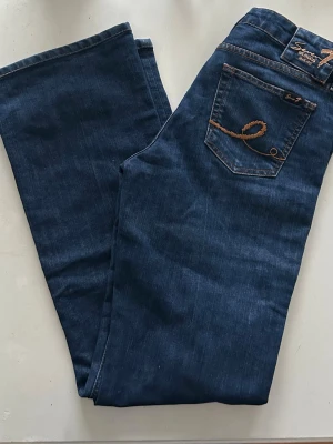 Mörkblå Seven7 jeans bootcut - Säljer ett par mörkblå jeans från Seven7 med klassisk bootcut-modell. Jeansen har snygga kontrastsömmar och broderade bakfickor med guldfärgad tråd. Tillverkade i mjukt jeansmaterial med lågmidjad passform och coola fickor.