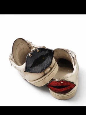 Vita sneakers med läppdetalj bak - Unika vita sneakers i skinn med snörning och coola läppar i blått och rött bak på hälen. Skorna har platt sula och rund tå, och detaljer i metall på läpparna. Perfekt för dig som vill sticka ut med din stil.