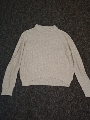 Beige ribbad stickad tröja - Mysig beige stickad tröja med ribbad struktur. Tröjan har långa ärmar och breda muddar vid ärmsluten.