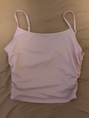 Ljusrosa linnetopp med smala band - Söt ljusrosa linnetopp med smala axelband och rynkade sidor. Toppen har en enkel, croppad passform och är perfekt för varma dagar.