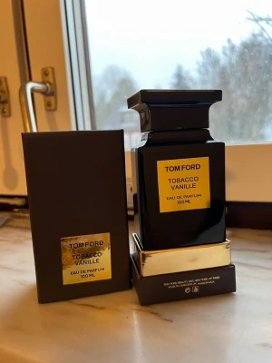 Tom Ford Tobacco Vanille EdP 100 ml - Tom Ford Tobacco Vanille Eau de Parfum 100 ml i en elegant svart glasflaska med guldfärgad etikett och detaljer. Flaskan har en fyrkantig form och kommer med originalkartong. En lyxig och ikonisk doft som kombinerar tobak och vanilj.