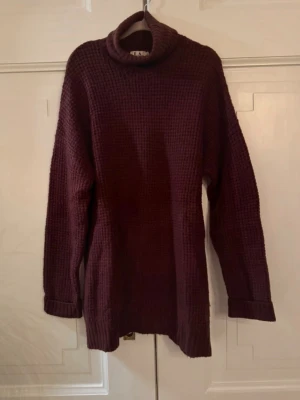 Vinröd polotröja i grovstickat - Mysig vinröd polotröja i grovstickat material med lång ärm och ribbade muddar. Tröjan har en avslappnad passform och hög polokrage som håller dig varm. Perfekt för lager på lager och höstiga outfits. Från kollektionen nakd x Linn Ahlborg