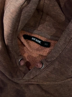 Rostbrun hoodie med magficka - Säljer en snygg rostbrun hoodie med huva och dragsko. Hoodien har en klassisk magficka och är tillverkad i mjukt, melerat tyg. Perfekt för en avslappnad och trendig stil.