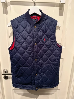 Marinblå quiltad dunväst Polo Ralph Lauren - Snygg marinblå dunväst från Polo Ralph Lauren med röd insida i stl 14-16 år. Pris kan diskuteras 