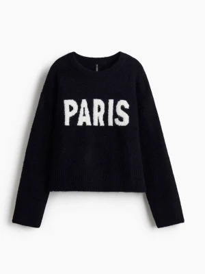 Svart stickad tröja med PARIS-tryck - Trendig svart stickad tröja med vit text 'PARIS' framtill. Tröjan har en croppad passform, rund halsringning och långa ärmar. Perfekt för dig som vill ha en cool statement-piece i garderoben.
