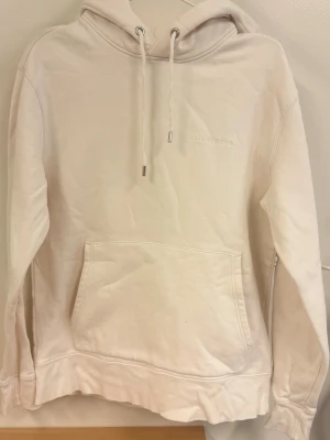J.Lindeberg hoodie - Snygg beige/vit hoodie från J.Lindeberg med broderad logga på bröstet. Hoodien har en stor känguruficka framtill, dragsko i huvan och ribbade muddar vid ärmar och nederkant. Väldigt fint skick!