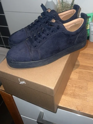Mörkblå mocka sneakers Louboutin - Snygga mörkblå sneakers från Christian Louboutin i mjuk mocka med klassisk röd sula och rund tå. Skorna har svarta snören och diskret logga på hälen. Perfekta för dig som vill ha något exklusivt och stilrent.storleken är 43 men passar även för lite större fötter,för fler frågor och funderingar hör av er✨