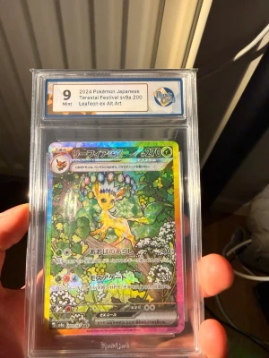 Leafeon ex Alt Art Pokémonkort 2024 - Japanskt Pokémonkort, Leafeon ex Alt Art från 2024 Terastal Festival sv8a 200. Kortet är graderat Mint 9 av RaukCard och har ett färgstarkt holografiskt motiv med Leafeon bland gröna blad och blommor. Kortet är inneslutet i ett skyddande plastfodral.