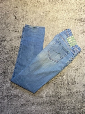 Ljusblåa Jacob Cohën jeans - Ett par riktigt feta Jacob Cohën jeans i storlek 33. Ljusblåa med gröna detaljer som det klassiska J - märket broderat på. Jeansen är i fint skick där den enda defekten är slitage på vänster ben samt vid gylfen, dock inga större fel som inte går att fixa! Hör gärna av dig vid minsta fundering🤝.