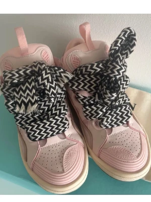 Lanvin curb rosa - Unika sneakers från Lanvin i ljusrosa mocka och skinn med kraftiga svartvita zigzag-mönstrade snören. Skorna har rund tå, perforerade detaljer och beige sula. Perfekt statement-piece för dig som gillar att sticka ut.