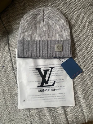 Grå mössa  - Snygg grå mössa med diskret rutmönster och ribbad kant. Märkt med metallbricka framtill. Tillverkad i mjuk ullmix som håller dig varm och stilren under kalla dagar. Perfekt accessoar för dig som gillar exklusiv streetstyle.