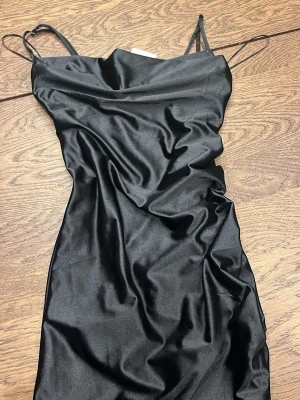 Svart satin klänning från Bik Bok - Snygg svart kort klänning från Bik Bok i glansigt satinliknande material. Klänningen har en figurnära passform och är perfekt för dig som gillar en stilren och trendig look. Helt ny! 
