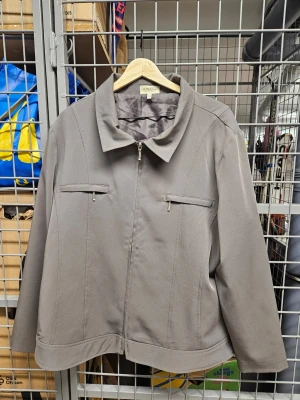 Grå jacka med dragkedja från Amalia - Snygg grå jacka från Amalia Collection i storlek 48. Jackan har rak passform, klassisk krage och dragkedja framtill. Två bröstfickor med dragkedja ger en clean look. Materialet känns mjukt och lätt, perfekt för vår och höst.