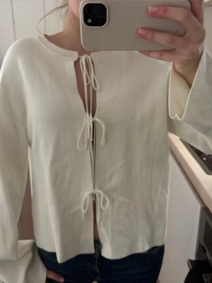 Vit kofta med knyt framtill - Säljer en superfin vit kofta med tre knyt framtill. Koftan har vida ärmar och är gjord i mjukt stickat material. Perfekt för lager på lager och ger en chill vibe till din outfit.