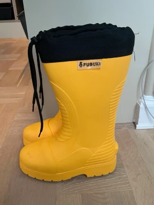 Gula FUBUKI stövlar med snörning - Säljer ett par riktigt coola gula FUBUKI stövlar med svart snörning upptill och svart greppig sula. Insidan är fodrad för extra värme och komfort. Perfekta för regniga dagar eller snöslask. Lite små i storleken