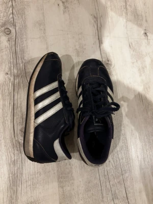 Adidas sneakers – mörkblå/silver, stl 37/39 - Snygga och klassiska vintage Adidas sneakers i mörkblått med silverfärgade ränder. Perfekta till vardags och lätt att matcha med olika outfits.   Märke: Adidas Storlek: EU 37 1/3 Färg: Mörkblå med silverdetaljer Skick: Använda, normalt slitage (se bilder). Inga större skador. Material: Skinn/konstläder 