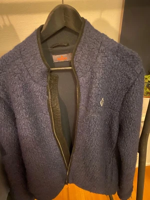 Mörkblå teddyjacka från Morris - Säljer en mörkblå teddyjacka från Morris i storlek M som är perfekt nu för vintern. Jackan har en mjuk och fluffig yta, dragkedja framtill och en snygg broderad logga på bröstet. Perfekt för dig som gillar stilren och bekväm look. Går att förhandla om priset. Så skriv om du är intresserad