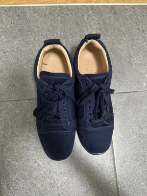 Mörkblå sneakers från Christian Louboutin - Säljer ett par mörkblå sneakers från Christian Louboutin i mocka med klassisk röd sula och broderad logga på hälen. Skorna har snörning och en platt sula, samt beige innersida i skinn. Perfekta för dig som vill sticka ut med exklusiva detaljer. Dom e använda men allt finns kvar, box o allt. Pris går att diskutera och om mer frågor de e ba att skriva.