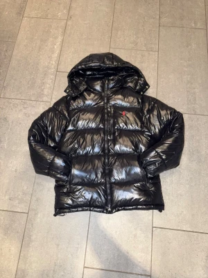 Ralph Lauren svart puffer jacka – blank finish – vinterjacka - Säljer en stilren och eftertraktad Polo Ralph Lauren puffer jacka i svart med blank finish. Jackan är varm, bekväm och perfekt för höst/vinter. Klassisk design som passar både casual och mer uppklädda outfits.  ✔ Original + kvitto 🧾(syns i bild) ✔ Mycket bra skick ✔ Tjock och varm ✔ Huva medföljer ✔ Dragkedja + fickor ✔ Snygg blank yta som ger ett premium och lyxigt utseende  Använd fåtal gånger, inga hål, inga fläckar eller defekter. Passar perfekt för dig som vill ha ett välvårdat  uppträdande