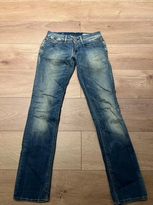 Replay jeana JENNPEZ - Säljer ett par blå jeans från Replay, modell JENNPEZ. W27 L32. De har snygg slitning, raka ben och coola detaljer som dragkedjor och pärlor på bakfickorna. Klassisk femficksmodell med låg midja och Replay-lapp bak. Perfekta till sneakers eller boots LOW RISE