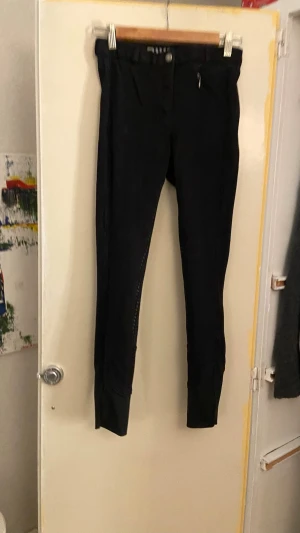 Svarta ridbyxor med helskoning - Säljer ett par svarta ridbyxor med helskoning i silikon för extra grepp. Byxorna har smal passform, bälteshällor och dragkedja fram. Helskoningen har ett prickigt mönster och materialet är stretchigt och bekvämt för ridning.