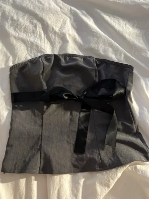 Black Strapless Corset Top with Bow 🎀 - Description: Black strapless corset-style top with a cute satin bow detail in the front. Gives a snatched fit and looks amazing with low-rise jeans or a skirt. Worn a few times and in good condition. No stains or flaws.  Perfect for going out, parties or a Y2K-inspired outfit ✨ Message me if you want more pictures or measurements!