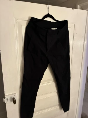 Svarta kostymbyxor från KappAhl - Snygga svarta kostymbyxor från KappAhl i storlek 38. Byxorna har raka ben, bälteshällor och diskreta fickor både fram och bak. Tillverkade i ett mjukt bomullsmaterial som känns bekvämt hela dagen.