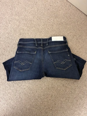 Replay mörkblå jeans - Säljer ett par mörkblå jeans från Replay med snygga kontrastsömmar och broderade bakfickor. Klassisk femficksmodell med bälteshällor och Replay-logga på bakre linningen. Jeansen är tillverkade i stretchig denim för skön passform.