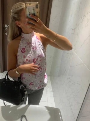 Blommig halterneck topp  - Säljer en söt halterneck topp i vitt med rosa och lila blommönster. Toppen har hög hals, öppen rygg och knyts i nacken. Storlek 38 men passar mig och jag brukar ha 36/S. Mycket fint skick🌸🌸