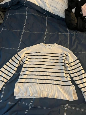 Randig stickad tröja från 157, M - Säljer en vit stickad tröja från 157 i storlek M med svarta ränder. Tröjan har bred ribbad mudd vid ärmslut och nederkant samt rund halsringning och slitsar längst ner på tröjan. Perfekt för dig som gillar klassisk och chill stil.