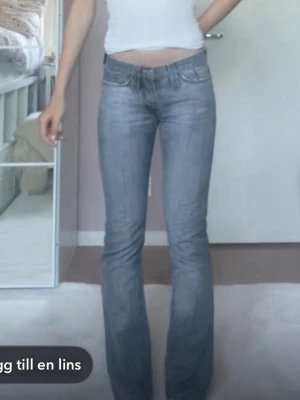 Vintage grå lågmidjade jeans xs-s - 🫶🏻Storlek: Jeansen är ca 5 cm för korta för mig som är 175 cm. Det är smala om låren. Skulle  passa någon runt 160-170.🫶🏻 💕Säljer ett par jättecoola vintage grå jeans från J.Lindeberg med klassisk femficksmodell och stora loggor på bakfickorna. Jeansen är bootcut och normal passform. Materialet är slitstarkt denim i bomull och färgen är snyggt tvättad grå. Rosa sömmar som ger gullig detalj💕⭐️Köpta secondhand för 300 kr.⭐️