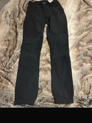 Svarta täckbyxor från Bergans XS - Säljer ett par svarta täckbyxor från Bergans i storlek XS. Byxorna har elastiska benslut, förstärkta knän och dragkedja samt knapp i midjan. Perfekta för vinteraktiviteter och outdoor. Materialet är slitstarkt och byxorna har en clean, sportig look.