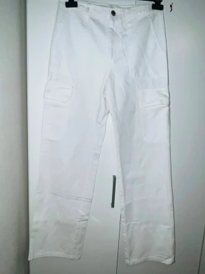 Vita cargobyxor från Zara - Säljer ett par vita cargobyxor från Zara med raka ben och stora djupa fickor på sidorna. Byxorna har hög midja, dragkedja och knapp framtill. Tillverkade i bomull. Perfekta till sneakers eller boots.