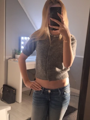 Grå croppad kofta med pärlor XS - Supersöt grå croppad kofta från H&M i stickad ullmix. Kort ärm och knappar framtill. Kragen är dekorerad med glittriga pärlor och stenar som ger extra bling. Perfekt till jeans eller kjol för en trendig look.