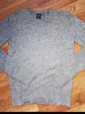 Grå stickad tröja från GAP med ull storlek xs,s kaschmir - Mysig grå stickad tröja från GAP med broderad logga framtill. Tröjan har rund halsringning, ribbade muddar vid ärmslut och nederkant samt lång ärm. Perfekt för kyliga dagar och enkel att matcha med jeans eller kjol.                                                                               Storlek Xs, men passar även S.                               Mycket fint skick!                                                            Djur och rökfritt hem 