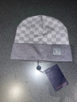 Grå rutig mössa  - Säljer en snygg grå mössa med klassiskt rutigt mönster. Mössan är stickad och har en bred uppvikt kant. Perfekt accessoar för dig som vill ha en stilren och exklusiv look.